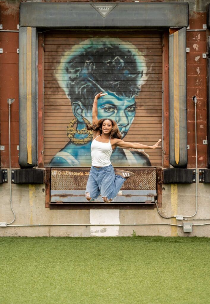 Action shot of a high school senior jumping in front of a stunning blue mural during a Charlotte Senior Signature Experience at Camp North End.