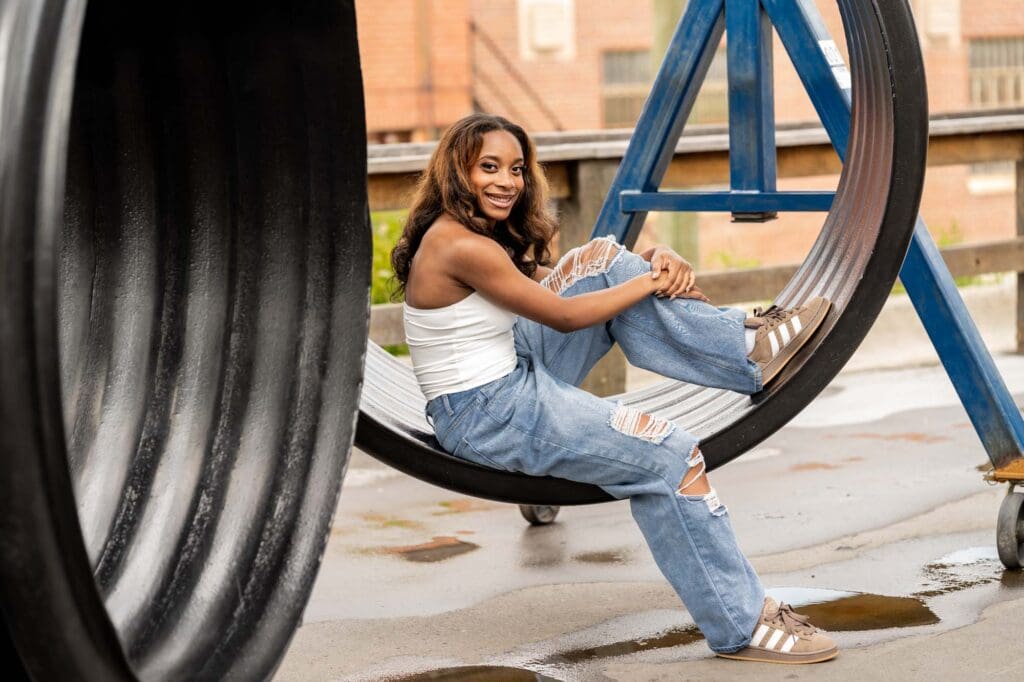 Creative portrait of a senior smiling and posing inside a large industrial hanging tire at Camp North End.