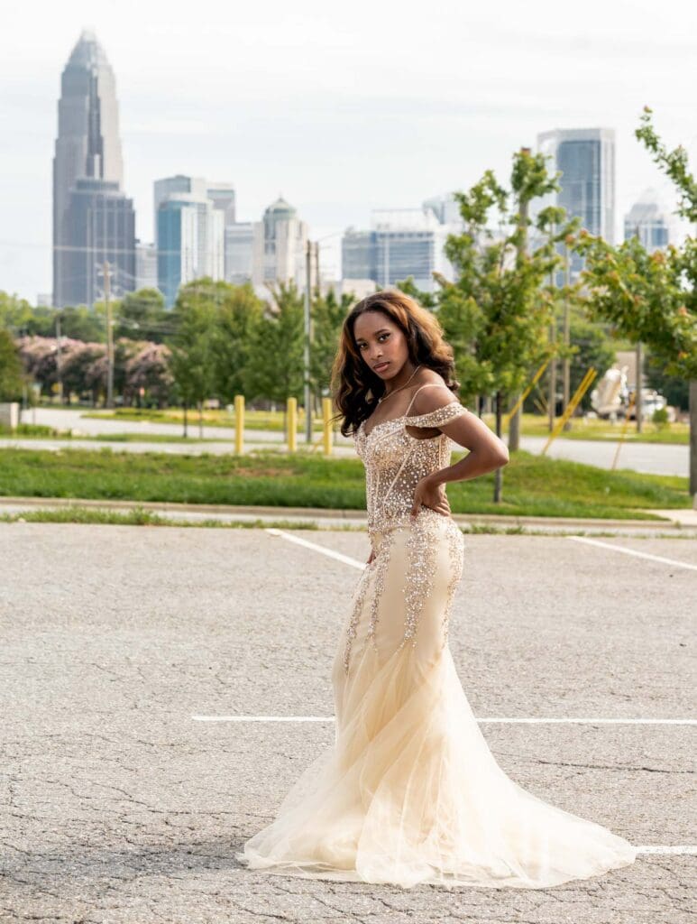 High school senior in a formal prom dress with the Charlotte skyline buildings in the background for a Charlotte Senior Signature Experience at Camp North End.