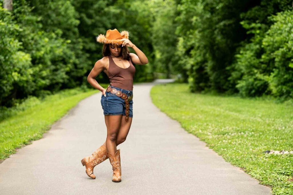High school senior posing on the greenway tipping her cowgirl hat during a Charlotte Senior Signature Experience at Goat Island Park.