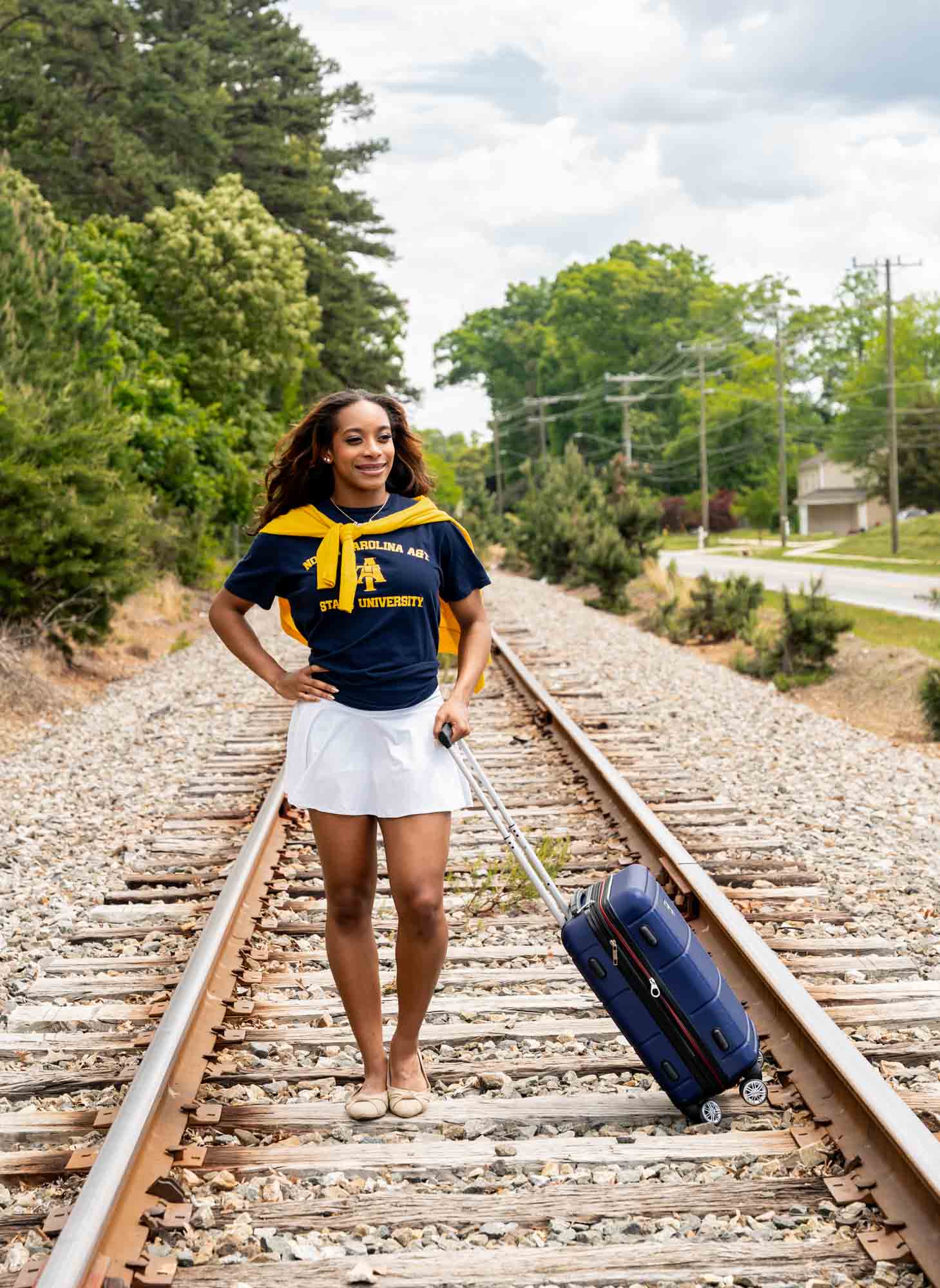 High school senior posing with luggage on train tracks wearing future college attire