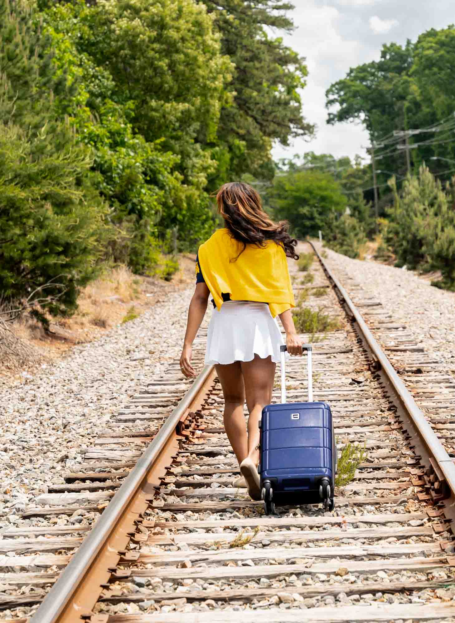 High school senior walking away with luggage on train tracks wearing future college attire