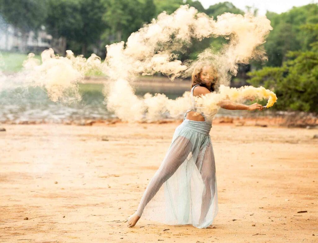 Action shot of high school senior dance choreography with explosive orange smoke along the Jetton Park waterfront shoreline.