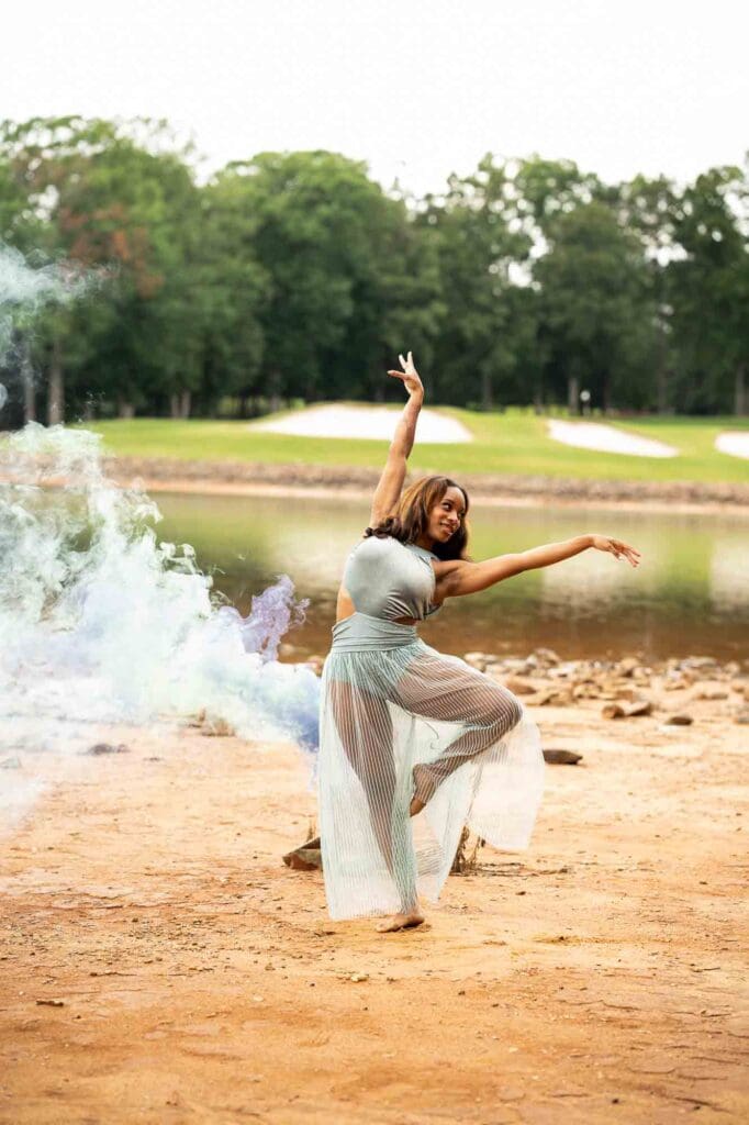 Dramatic waterfront portrait of a senior dancer posing with blue and purple smoke bombs for a Charlotte Senior Signature Experience at Jetton Park.